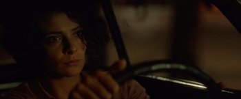 Movie still from “The Gunman” (2015), directed by Pierre Morel – A woman sitting in the driver's seat of a car at night; Close Up shot, Over the shoulder angle