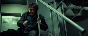 Movie still from “The Gunman” (2015), directed by Pierre Morel – A man sitting on top of a metal railing; Medium shot, Low angle