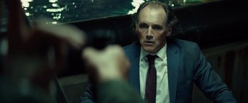 Movie still from “The Gunman” (2015), directed by Pierre Morel – A man in a suit and tie sitting in a car; Close Up shot, Over the shoulder angle