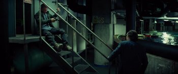 Movie still from “The Gunman” (2015), directed by Pierre Morel – Two people are sitting on some stairs in a dark room; Wide shot, High angle