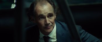 Movie still from “The Gunman” (2015), directed by Pierre Morel – A person wearing a suit and tie; Close Up shot, Over the shoulder angle