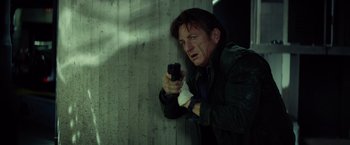 Movie still from “The Gunman” (2015), directed by Pierre Morel – A man holding a gun in his hand; Medium shot, Low angle