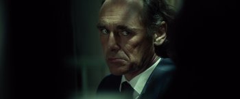 Movie still from “The Gunman” (2015), directed by Pierre Morel – A man in a suit and tie looking at the camera; Close Up shot, Over the shoulder angle