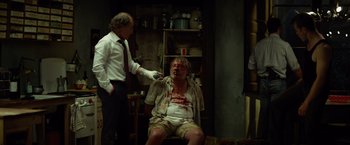 Movie still from “The Gunman” (2015), directed by Pierre Morel – A man is shaving another man's head in a room; Medium shot, Over the shoulder angle