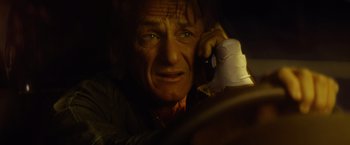 Movie still from “The Gunman” (2015), directed by Pierre Morel – A person sitting in a car on the phone; Close Up shot, High angle
