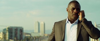 Movie still from “The Gunman” (2015), directed by Pierre Morel – A man wearing a suit and tie standing in front of a city; Close Up shot, Low angle