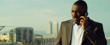 Movie still from “The Gunman” (2015), directed by Pierre Morel – A man wearing a suit and tie standing in front of a city; Close Up shot, Low angle