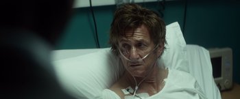 Movie still from “The Gunman” (2015), directed by Pierre Morel – A person laying in a hospital bed; Close Up shot, Over the shoulder angle