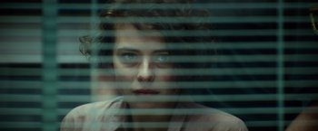 Movie still from “The Gunman” (2015), directed by Pierre Morel – A woman looking out a window through blinds; Close Up shot, Over the shoulder angle