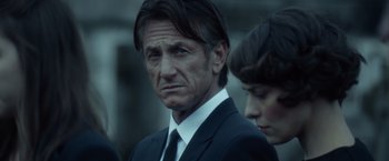 Movie still from “The Gunman” (2015), directed by Pierre Morel – A man in a suit and tie next to a woman in a suit; Close Up shot, Over the shoulder angle