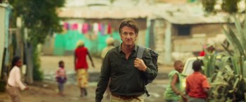 Movie still from “The Gunman” (2015), directed by Pierre Morel – A man in a black shirt is walking down the street; Medium shot, Over the shoulder angle