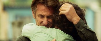 Movie still from “The Gunman” (2015), directed by Pierre Morel – A man and a woman hugging each other; Close Up shot, Over the shoulder angle
