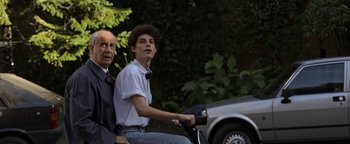 Movie still from “The Hand of God” (2021), directed by Paolo Sorrentino – An older man and a young man riding a bike; Medium shot, Low angle
