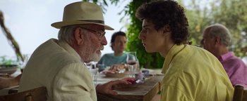 Movie still from “The Hand of God” (2021), directed by Paolo Sorrentino – Two men are sitting at a table talking to each other; Close Up shot, Over the shoulder angle