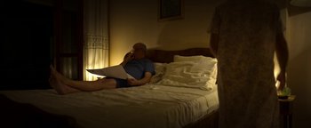 Movie still from “The Hand of God” (2021), directed by Paolo Sorrentino – A man sitting on top of a bed with a laptop computer; Medium shot, High angle