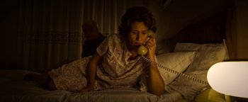 Movie still from “The Hand of God” (2021), directed by Paolo Sorrentino – An older woman sitting on a bed talking on the phone; Medium shot, High angle