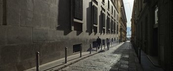 Movie still from “The Hand of God” (2021), directed by Paolo Sorrentino – A group of people walking down a sidewalk near a tall building; Extreme Wide shot, High angle