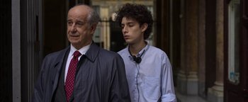 Movie still from “The Hand of God” (2021), directed by Paolo Sorrentino – A man and a man in a suit standing next to each other; Medium shot, Over the shoulder angle