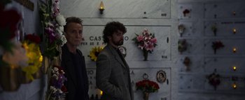 Movie still from “The Hand of God” (2021), directed by Paolo Sorrentino – Two men standing next to each other in front of a wall of flowers; Medium shot, Low angle