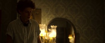 Movie still from “The Hand of God” (2021), directed by Paolo Sorrentino – A person standing in a room with a lamp in the background; Medium shot, Over the shoulder angle