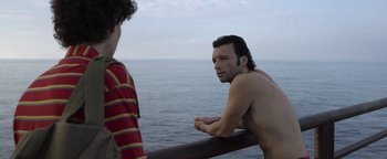 Movie still from “The Hand of God” (2021), directed by Paolo Sorrentino – A man standing next to another man near the ocean; Medium shot, Over the shoulder angle