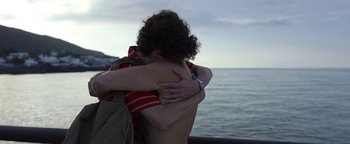 Movie still from “The Hand of God” (2021), directed by Paolo Sorrentino – A man hugging another man on the beach; Medium shot, Over the shoulder angle