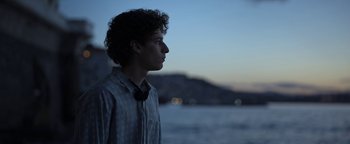 Movie still from “The Hand of God” (2021), directed by Paolo Sorrentino – A young man standing in front of a body of water at dusk; Medium shot, Low angle