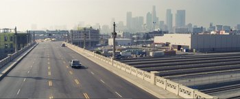 Movie still from “The Happytime Murders” (2018), directed by Brian Henson – A car driving down a street next to a train station; Extreme Wide shot, High angle
