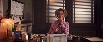 Movie still from “The Happytime Murders” (2018), directed by Brian Henson – A woman sitting at a desk talking on a phone; Medium shot, High angle