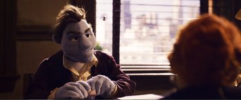 Movie still from “The Happytime Murders” (2018), directed by Brian Henson – A person wearing a suit and tie sitting at a table; Medium shot, Over the shoulder angle