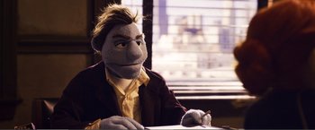 Movie still from “The Happytime Murders” (2018), directed by Brian Henson – A person with a stuffed animal sitting at a table; Medium shot, Over the shoulder angle