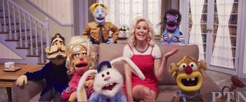 Movie still from “The Happytime Murders” (2018), directed by Brian Henson – A woman sitting on top of a couch next to a bunch of puppets; Medium shot, High angle