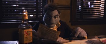 Movie still from “The Happytime Murders” (2018), directed by Brian Henson – A person sitting at a table with a stuffed animal; Medium shot, Over the shoulder angle