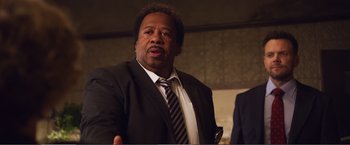 Movie still from “The Happytime Murders” (2018), directed by Brian Henson – A man in a suit and tie talking to a crowd; Close Up shot, Over the shoulder angle