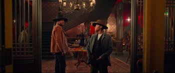 Movie still from “The Harder They Fall” (2021), directed by Jeymes Samuel – Two men in hats and jackets talking in a room; Wide shot, Low angle