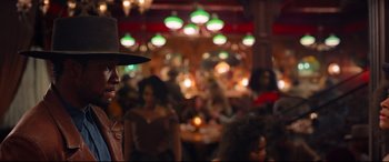 Movie still from “The Harder They Fall” (2021), directed by Jeymes Samuel – A crowd of people sitting at tables in a restaurant; Medium shot, Over the shoulder angle