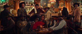 Movie still from “The Harder They Fall” (2021), directed by Jeymes Samuel – A group of people sitting at a table with a fan; Wide shot, High angle