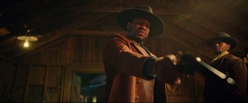 Movie still from “The Harder They Fall” (2021), directed by Jeymes Samuel – A man wearing a hat and a long coat; Medium shot, Low angle