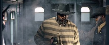 Movie still from “The Harder They Fall” (2021), directed by Jeymes Samuel – A man wearing a hat and a striped jacket; Medium shot, Low angle