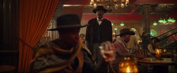 Movie still from “The Harder They Fall” (2021), directed by Jeymes Samuel – A man standing in a room with a hat on his head; Medium shot, Over the shoulder angle