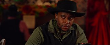 Movie still from “The Harder They Fall” (2021), directed by Jeymes Samuel – A man wearing a black hat and a green vest; Close Up shot, Over the shoulder angle