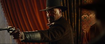 Movie still from “The Harder They Fall” (2021), directed by Jeymes Samuel – A man in a black hat and a brown jacket; Medium shot, Low angle