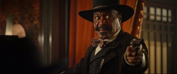 Movie still from “The Harder They Fall” (2021), directed by Jeymes Samuel – An older man wearing a hat and a bow tie; Close Up shot, Low angle