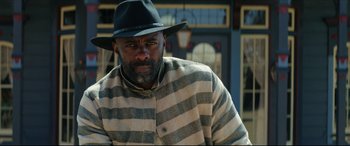 Movie still from “The Harder They Fall” (2021), directed by Jeymes Samuel – A man wearing a striped jacket and a black hat; Medium shot, Low angle