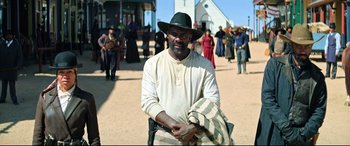 Movie still from “The Harder They Fall” (2021), directed by Jeymes Samuel – A man wearing a black hat standing in front of a crowd of onlookers; Medium shot, Over the shoulder angle