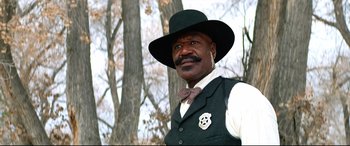 Movie still from “The Harder They Fall” (2021), directed by Jeymes Samuel – A man wearing a black hat and a vest; Medium shot, Low angle