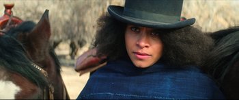 Movie still from “The Harder They Fall” (2021), directed by Jeymes Samuel – A woman in a black hat is holding her hair; Close Up shot, Low angle