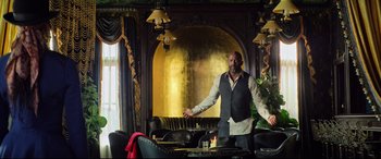 Movie still from “The Harder They Fall” (2021), directed by Jeymes Samuel – A man standing in front of a table in a room; Medium shot, Low angle
