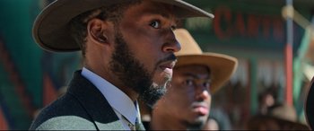 Movie still from “The Harder They Fall” (2021), directed by Jeymes Samuel – A man with a beard wearing a hat and a suit; Close Up shot, Over the shoulder angle