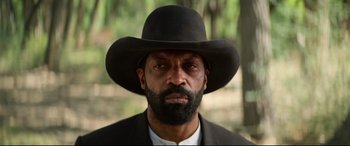 Movie still from “The Harder They Fall” (2021), directed by Jeymes Samuel – A man with a beard wearing a black hat; Close Up shot, Low angle